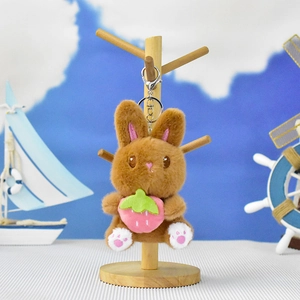 Cute brown plush bunny keychain holding a pink strawberry on a display stand