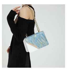 Detail of blue and white crossbody bag with wave pattern and golden chain strap on model