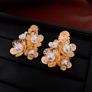 Detail of golden textured floral earrings with white pearls on black jewelry display