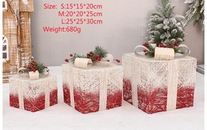Three gradient red and white lighted Christmas gift boxes with pine cones and berries