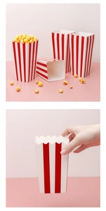 Close-up of red and white striped popcorn boxes being held and filled on a pink background