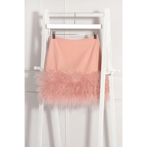 Détail de jupe courte rose avec garniture en plumes sur un support en bois blanc