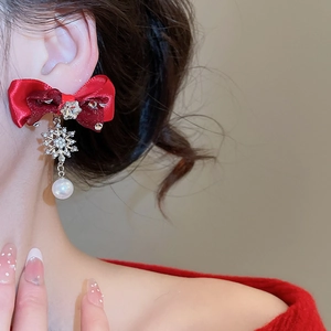 Close-up of red ribbon bow earrings with silver snowflake and pearl drop on model
