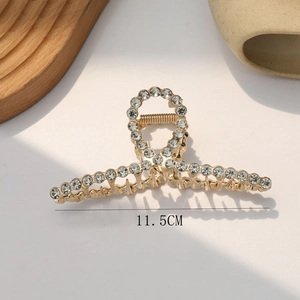 Detail shot of a 11.5cm golden metal hair claw clip with rhinestones and pearl design