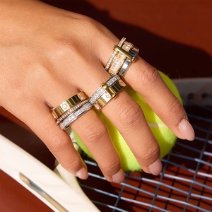 Détail de bagues superposées en or et argent avec zircons sur fond de court de tennis