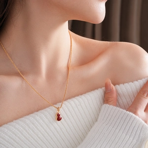 Close-up of gold-plated necklace with a red gourd pendant worn on the neck