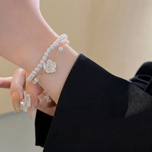 Elegant double-layer pearl bracelet with gold camellia pendant shown on a model