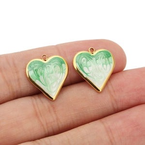 Close-up of green marble enamel heart pendants with gold plating held between fingers