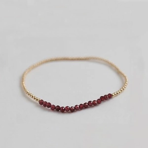 Close-up of minimalist beaded bracelet with faceted red stones and gold metal spacers