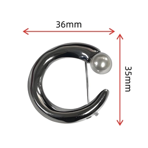 Detailed view of C-shaped metal brooch with pearl inlay, measuring 36mm by 35mm