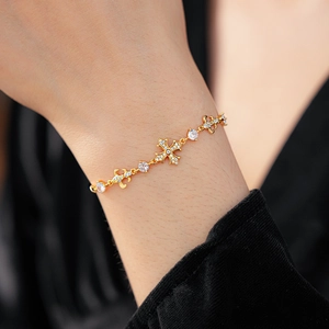Détail d'un bracelet croix doré avec diamants et perles scintillantes sur le poignet