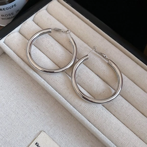 Close-up of polished silver hoop earrings displayed on a cream velvet jewelry tray
