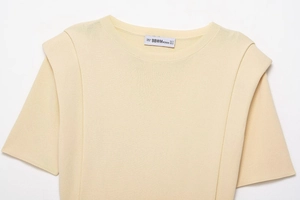 Detailed view of beige crew neck knit top with shoulder pads and woven neck label