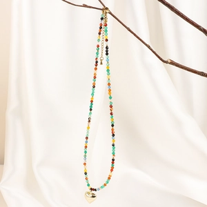 Detail of colorful beads and gold heart pendant hanging on a natural tree branch