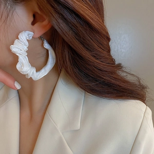 Detail of white pleated fabric hoop earring on model showing elegant texture and style