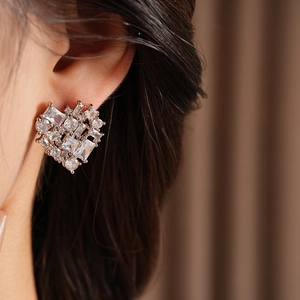 Close-up of heart-shaped silver earrings with square zircon stones worn by a model