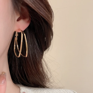 Close-up of model wearing double-layered golden textured hoop earrings with metallic finish