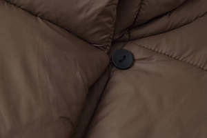 Détail d'un bouton rond noir sur une doudoune matelassée marron au fini satiné