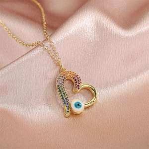 Détail d'un pendentif cœur doré avec pierres arc-en-ciel et œil maléfique sur satin