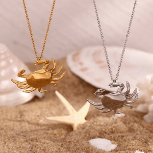 Detailed shot of gold and silver crab necklaces on a beach setting with seashells