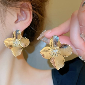 Exaggerated golden flower earrings with zircon center and brushed metal finish on model