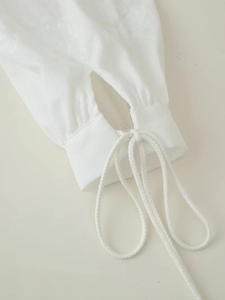 Detail of white cotton linen shirt sleeve featuring intricate lace-up cuff and textured fabric