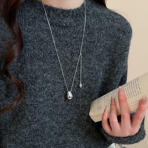 Detail of minimalist teardrop pendant on grey knit sweater with a smooth metallic finish