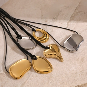 Irregular gold and silver pendants on black cords displayed on a stone surface