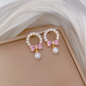 Macro detail of bow-knot pearl earring with pink zircon inlay and golden finish