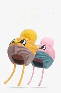 Detail of warm winter knit ear-flap hats with pom-poms and cartoon embroidery