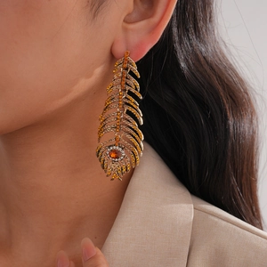 Détail de boucles d'oreilles plume dorées vintage avec strass jaunes et blancs brillants