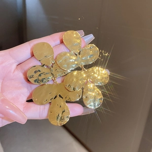 Close-up of oversized gold-finished hammered metal fan earrings with leaf textures