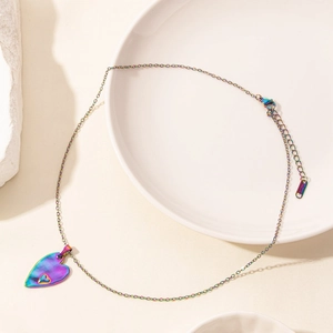 Iridescent heart pendant necklace in rainbow finish displayed on a white ceramic plate