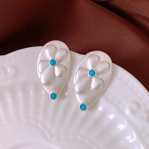 Detail of silver drop earrings with floral relief and turquoise beads on ceramic