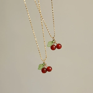Elegant gold chain necklace with red carnelian cherry pendant on grey background