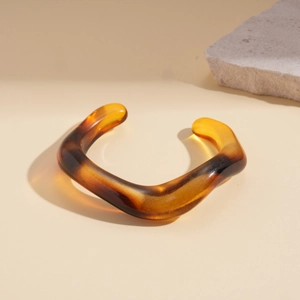 Detail of amber acrylic wavy bangle showing resin texture and irregular geometric design