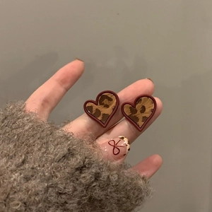 Close-up of heart-shaped leopard print earrings with a glossy finish and red border