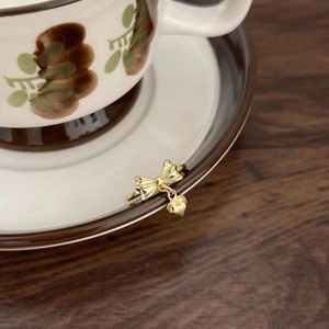 Golden bow heart ring hanging on a vintage ceramic cup edge with wooden background