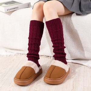 Detail of burgundy cable knit leg warmers paired with brown plush slippers in a home setting