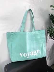 Detail shot of mint green canvas tote bag featuring white voyage lettering on a leather chair