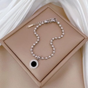 Detail of silver beaded bracelet with black round pendant on white silk background
