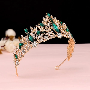 Close-up of golden Baroque crown with green gemstones and white crystals on a soft background
