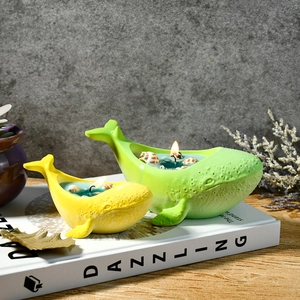 Whale-shaped scented candle set in yellow and green with seashell details on a book