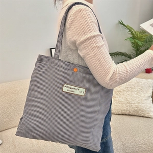 Detail of blue plaid tote bag featuring canvas patch with smiley face and orange button