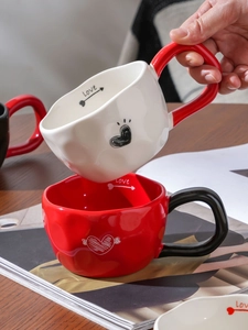 Close-up of ceramic heart mugs with Love lettering and winged heart design on wooden table