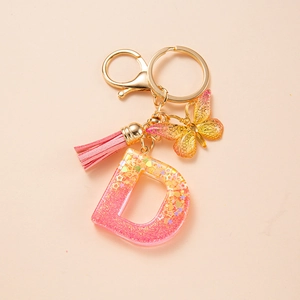 Detail of pink resin letter D keychain with golden butterfly and soft tassel