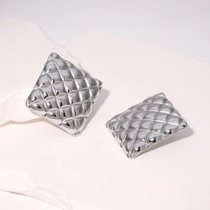 Close-up of silver quilted rhombus pattern earrings on white decorative stone base