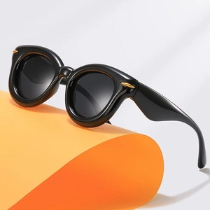Thick black round sunglasses with gold rivets on orange display prop, modern style