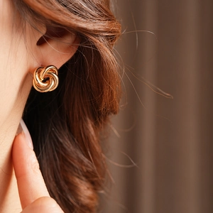 Close-up of elegant gold twisted knot stud earrings worn by a model in soft lighting