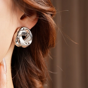 Gros plan de boucles d'oreilles nœud en argent portées par un mannequin au style chic